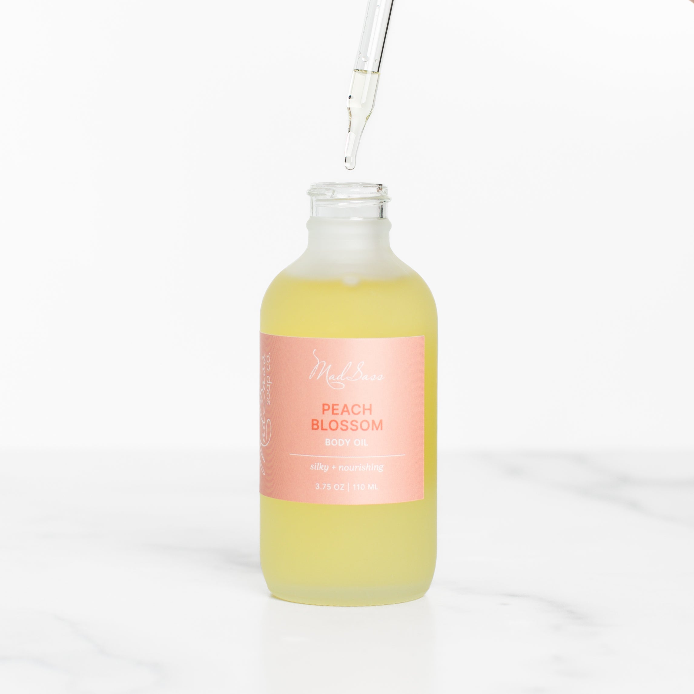 Close-up of the dropper dispensing Peach Blossom skin nourishing body oil by Mad Sass Soap Co, emphasizing the luxurious texture and golden hue.