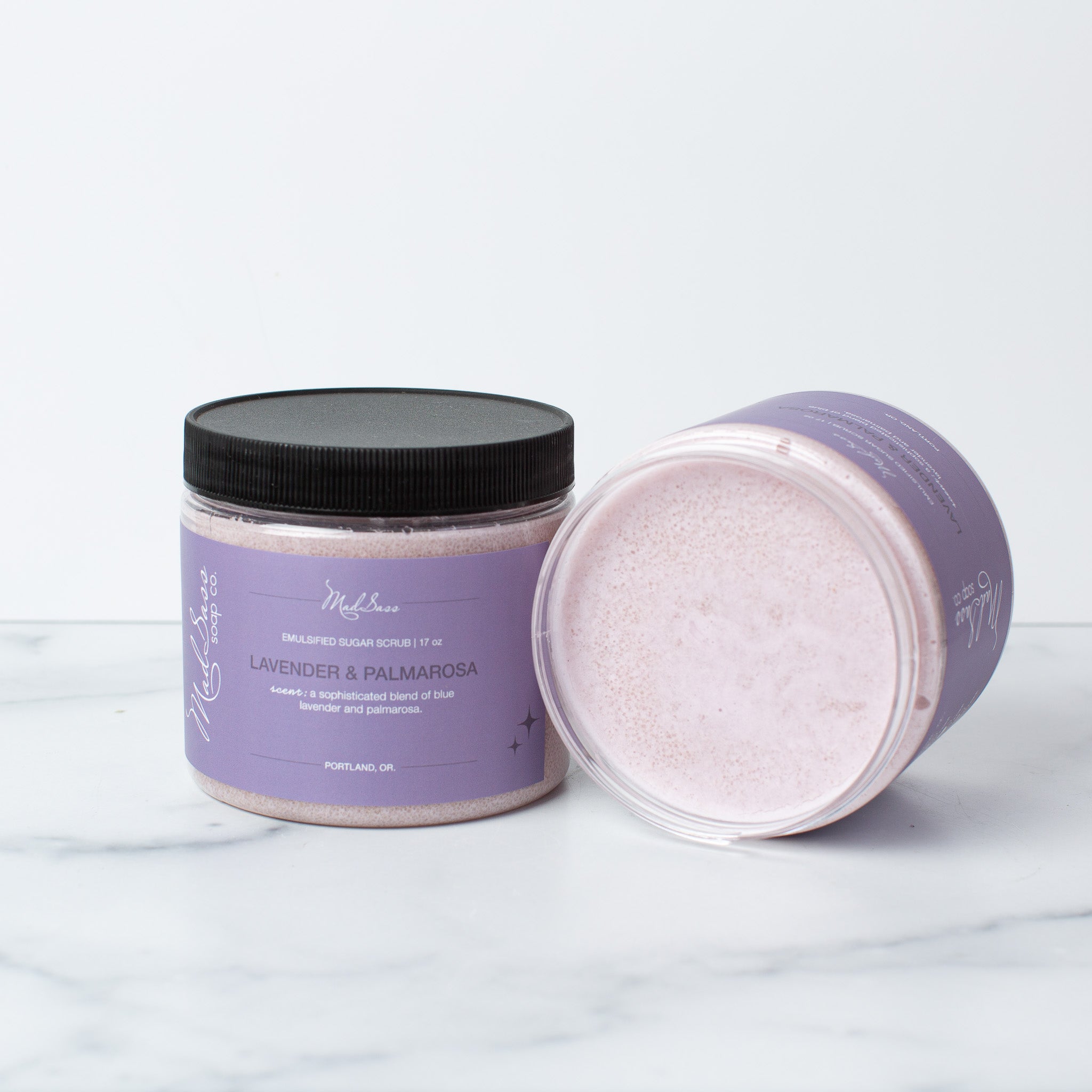 Two Lavender & Palmarosa Emulsified Sugar Scrubs, with one on its side, on a white background.