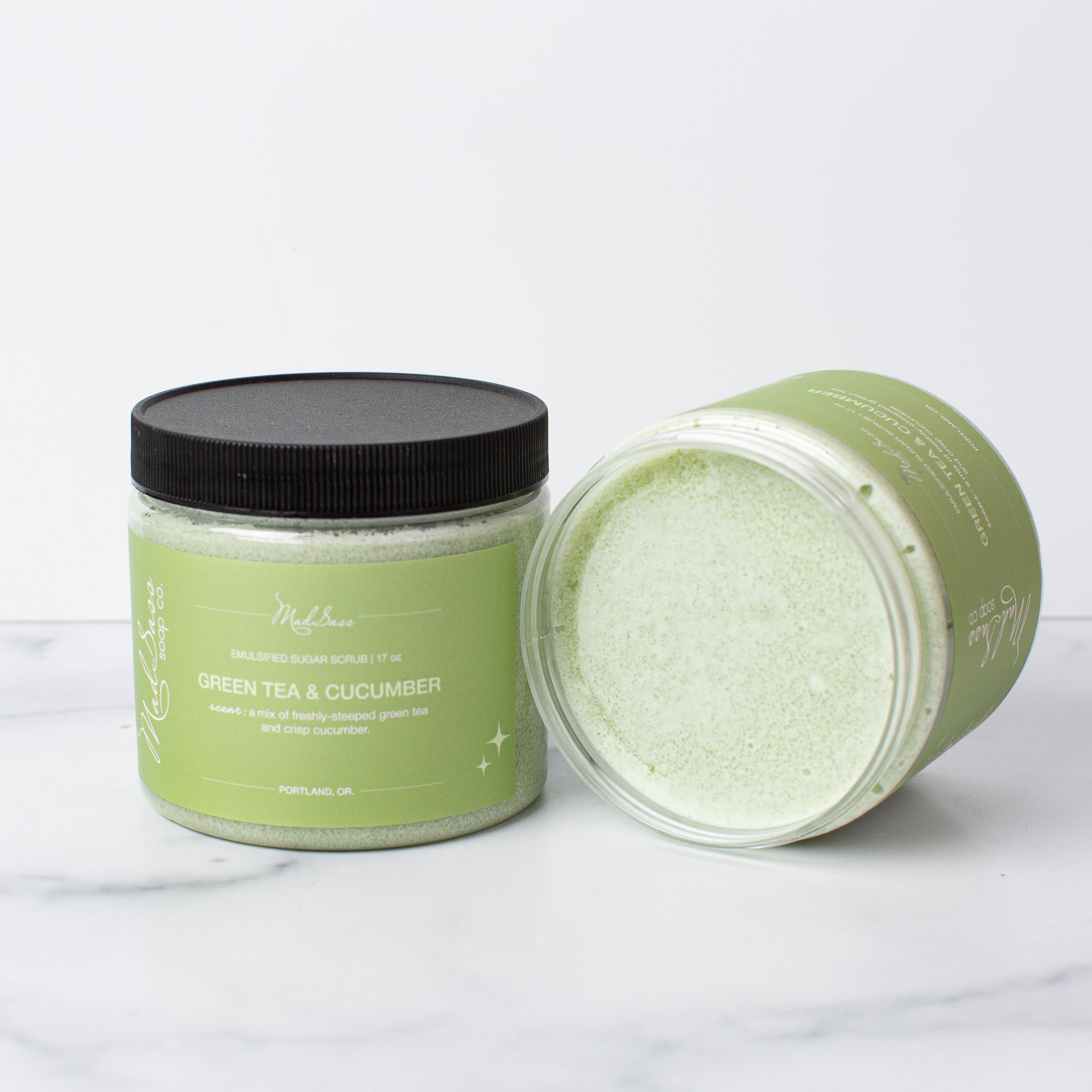 Two Green Tea & Cucumber Emulsified Sugar Scrubs, with one on its side, on a white background.