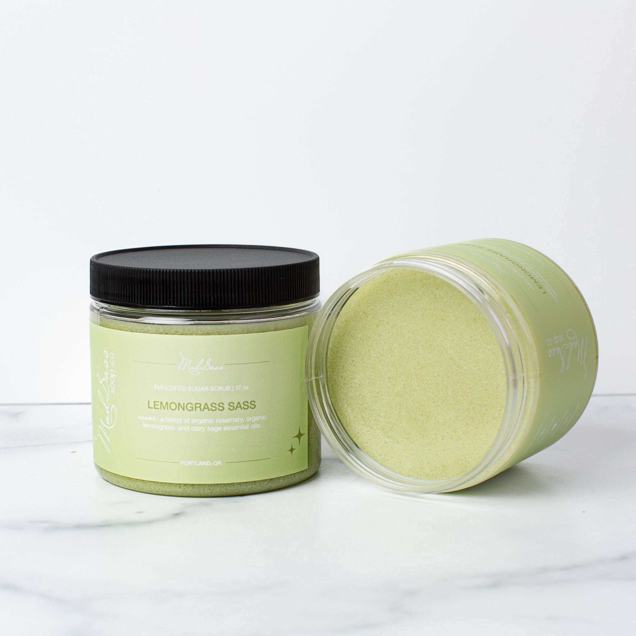 Two Lemongrass Sass Emulsified Sugar Scrubs, with one on its side, on a white background.