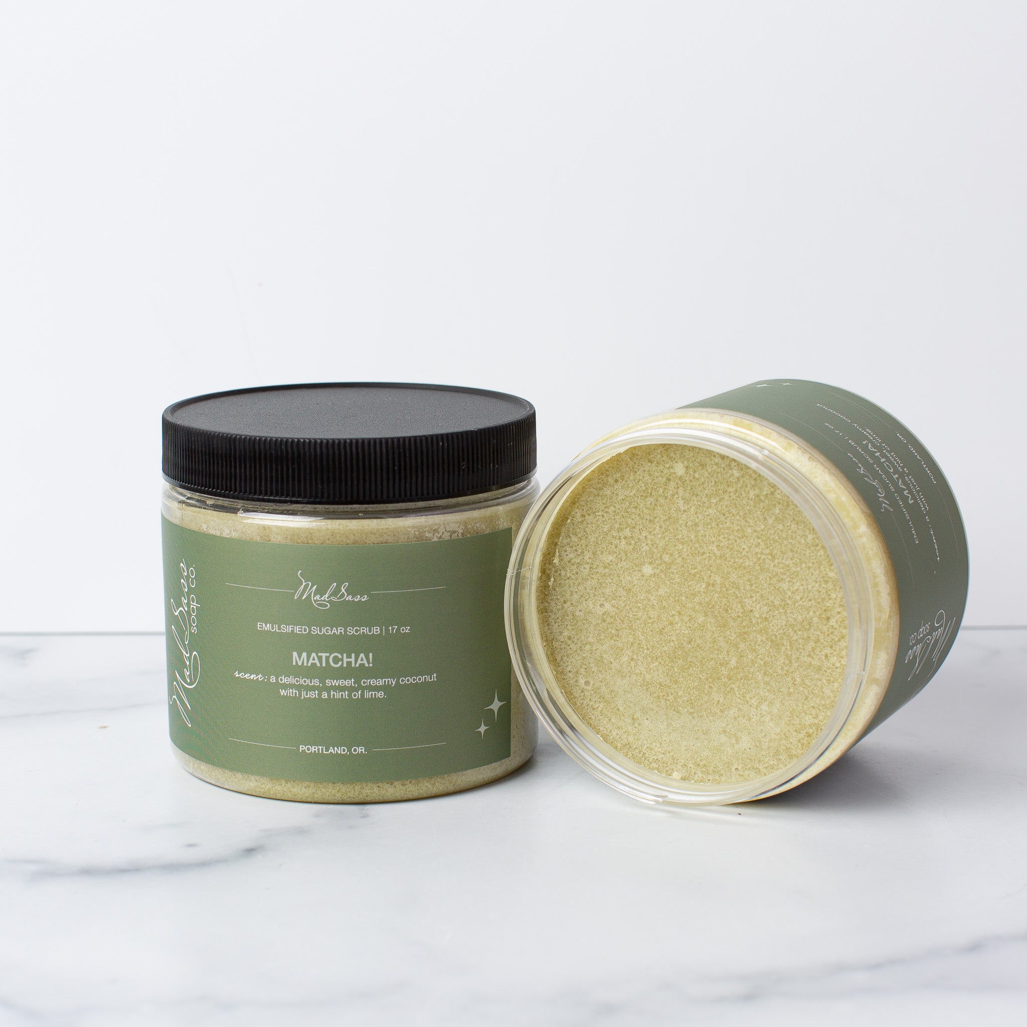 Two Matcha Emulsified Sugar Scrubs, with one on its side, on a white background.