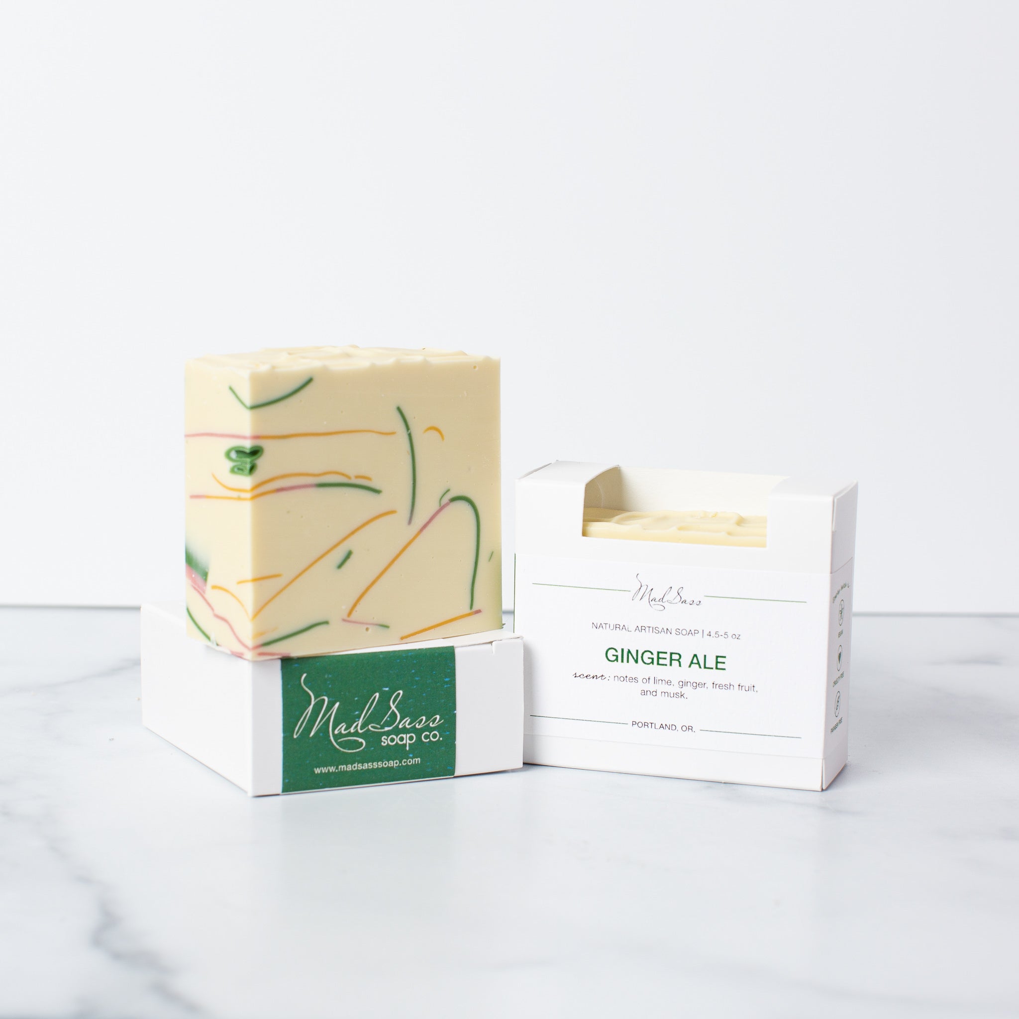Two boxes of Ginger Ale soap and a bar of Ginger Ale soap on a white background. Ginger Ale is a creamy-white soap with green, yellow, and pink soap shavings embedded.