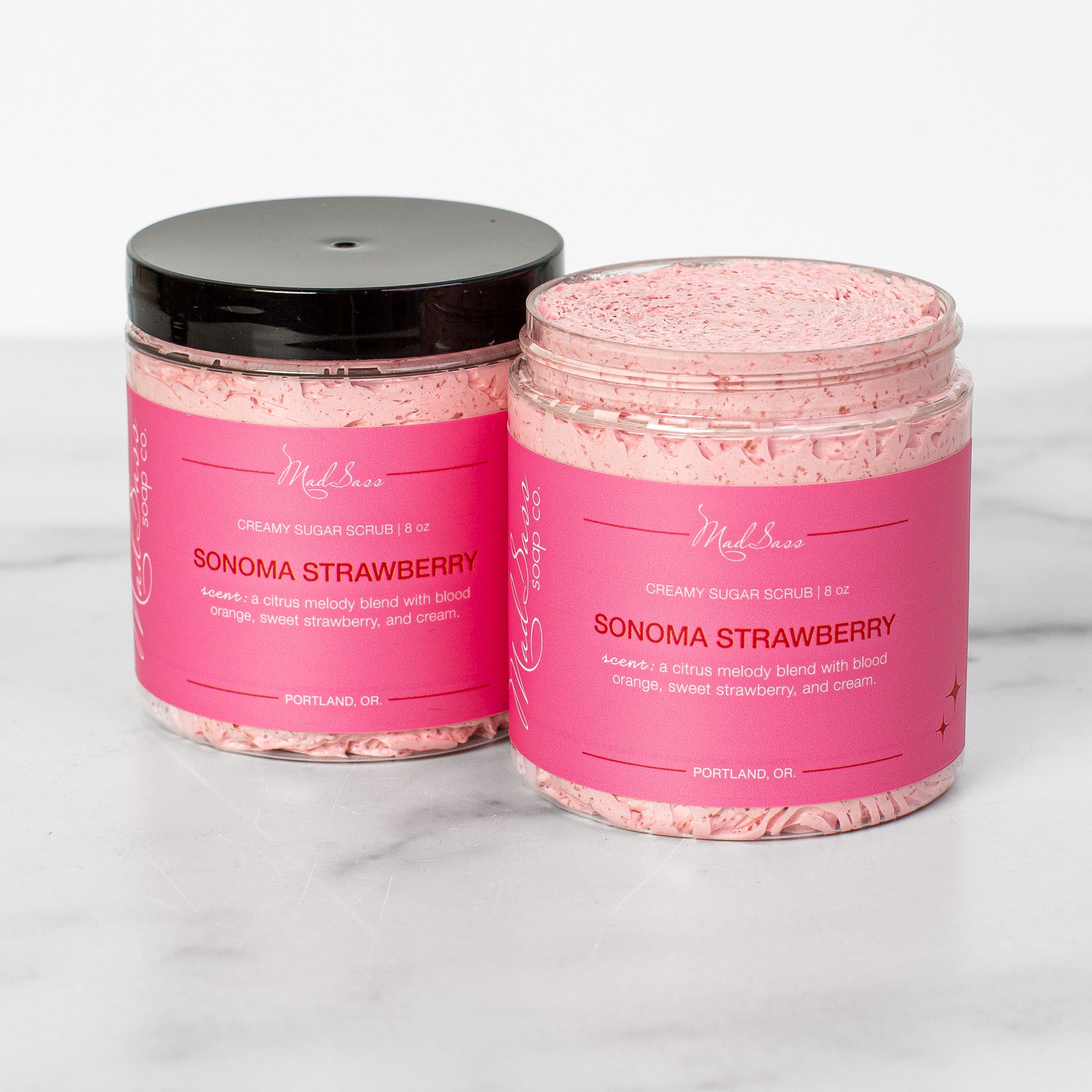 Two containers of Sonoma Strawberry Creamy Sugar Scrubs on a white background. Sonoma Strawberry is a light pink scrub in a clear tub.