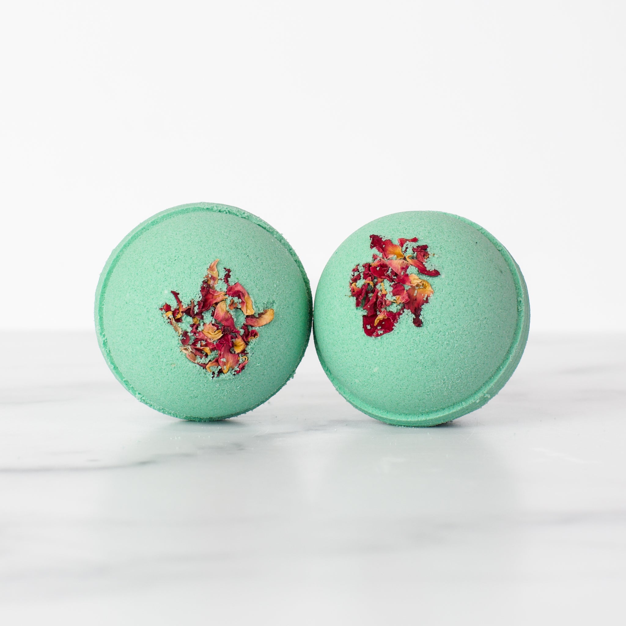 A pair of stylish Fog & Rose hydrating luxury bath bombs by Mad Sass Soap Co, showcasing a beautiful turquoise hue with floral accents for a luxurious bath experience.