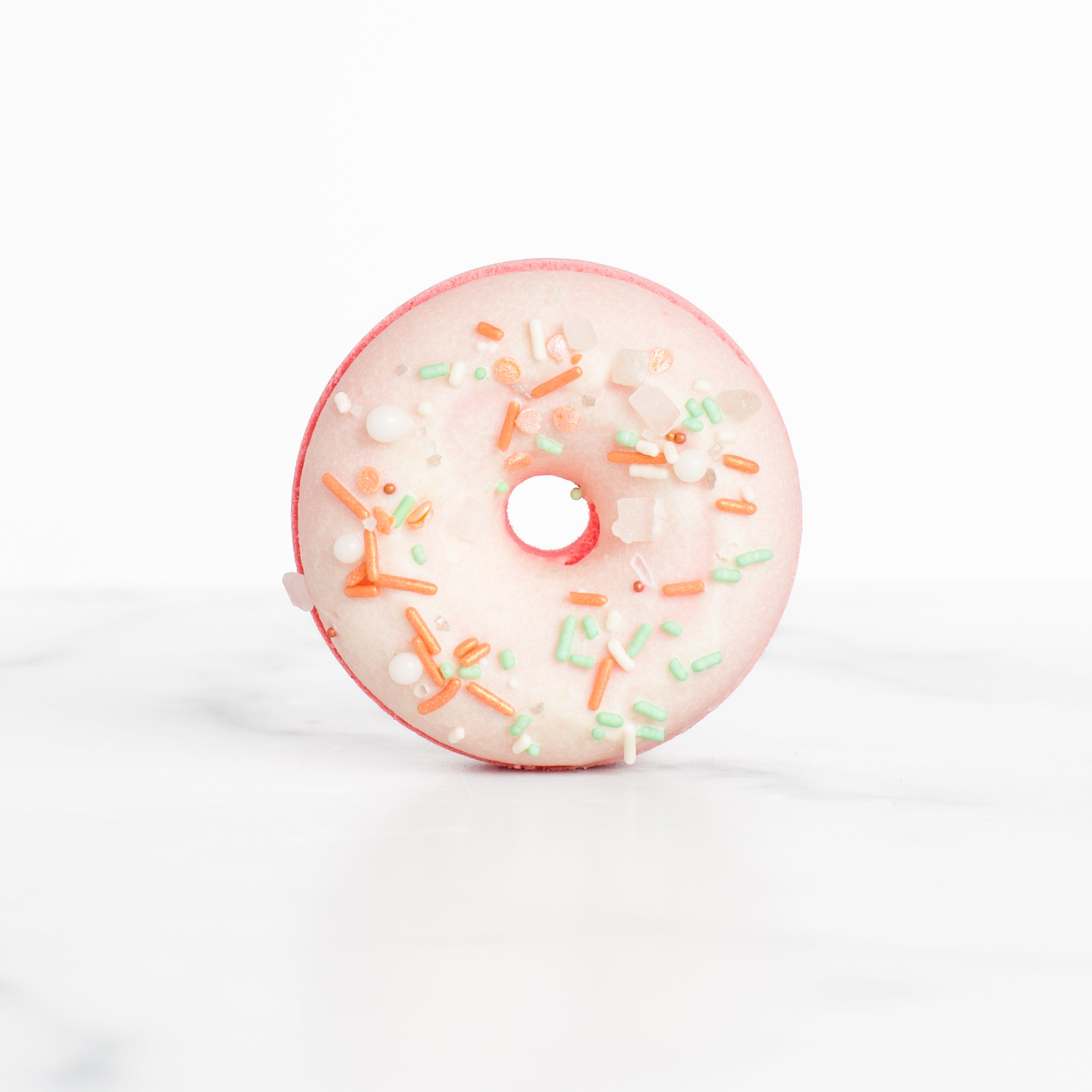 A close-up view of the Peach Blossom bath bomb by Mad Sass Soap Co, shaped like a pink donut with vibrant sprinkles, ideal for a hydrating luxury bath indulgence.