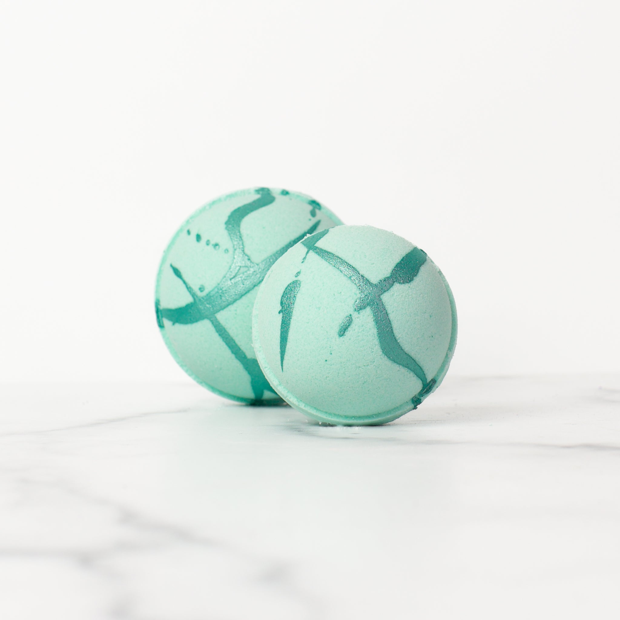 Two Spa Day bath bombs by Mad Sass Soap Co arranged artistically, featuring a stunning teal swirl design, perfect for enhancing your bath time with a touch of luxury.