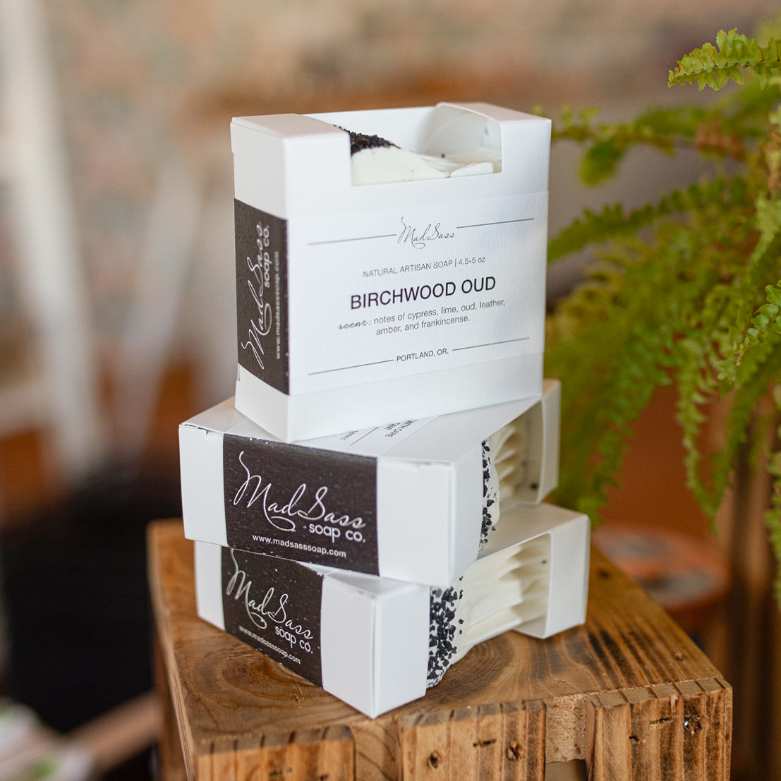 Three boxes of Birchwood Oud soap stacked on top of each other on a wooden block.